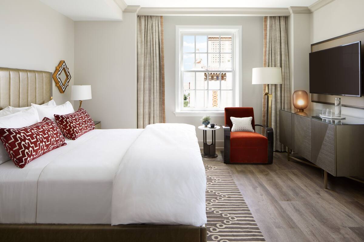 A hotel room with a large bed, a desk, a chair, a TV, and a window with curtains.