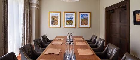 Een congreszaal met een lange tafel, lederen stoelen, een kroonluchter en ingelijste foto's aan de muur.