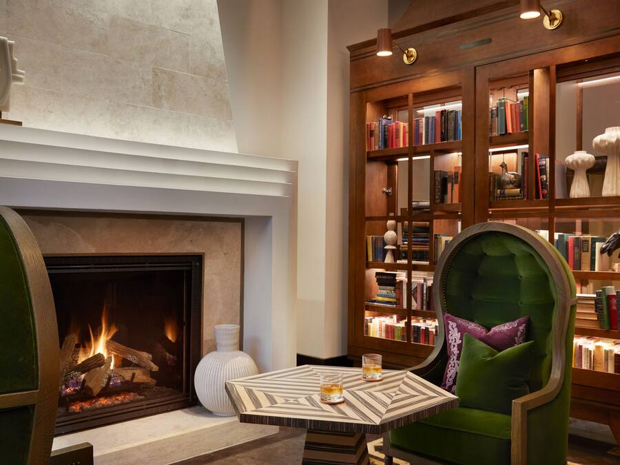 A cozy library with a fireplace, bookshelves, and a comfortable reading chair.