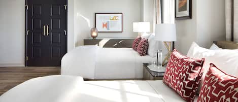 A hotel room with a large bed, a bedside table with a lamp, a framed artwork on the wall, and a dark door.