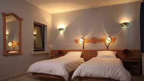 Une chambre avec deux lits simples, un grand miroir et des lampes de lecture fixées au mur.