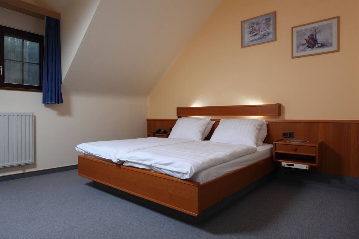 A bedroom with a wooden bed, a nightstand, a dresser, and a window with curtains.