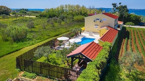 Une maison à deux étages avec une piscine, entourée d’un jardin clos et de champs.