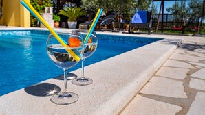 Deux verres contenant un liquide transparent, avec des pailles jaunes et bleues, une fleur et une scène se déroulant au bord d’une piscine.