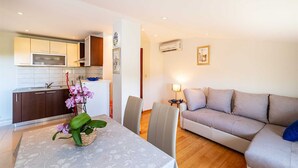 Un salon moderne avec un canapé beige, une table à manger avec des chaises et un coin cuisine équipé de placards et d’un four à micro-ondes.