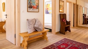 Une pièce dotée d’un plancher en bois, d’un banc agrémenté de coussins, d’un tapis rouge à motifs et d’œuvres d’art encadrées accrochées aux murs.