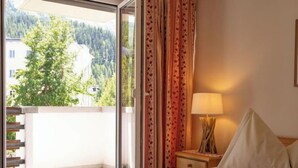 Une chambre d’hôtel avec un lit, une table de chevet, une lampe et une vue sur une forêt, visible à travers une porte coulissante.