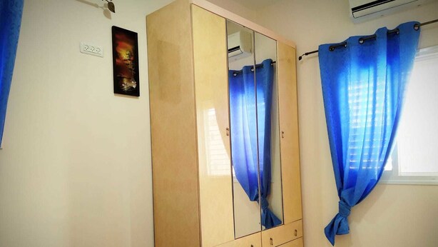 Ein Schlafzimmer mit einem Bett, einem Kleiderschrank, einem Spiegel und einem Fenster mit blauen Vorhängen.