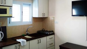 Eine kompakte Küche mit Mikrowelle, Spüle, Schränken und einem an der Wand montierten Fernseher.