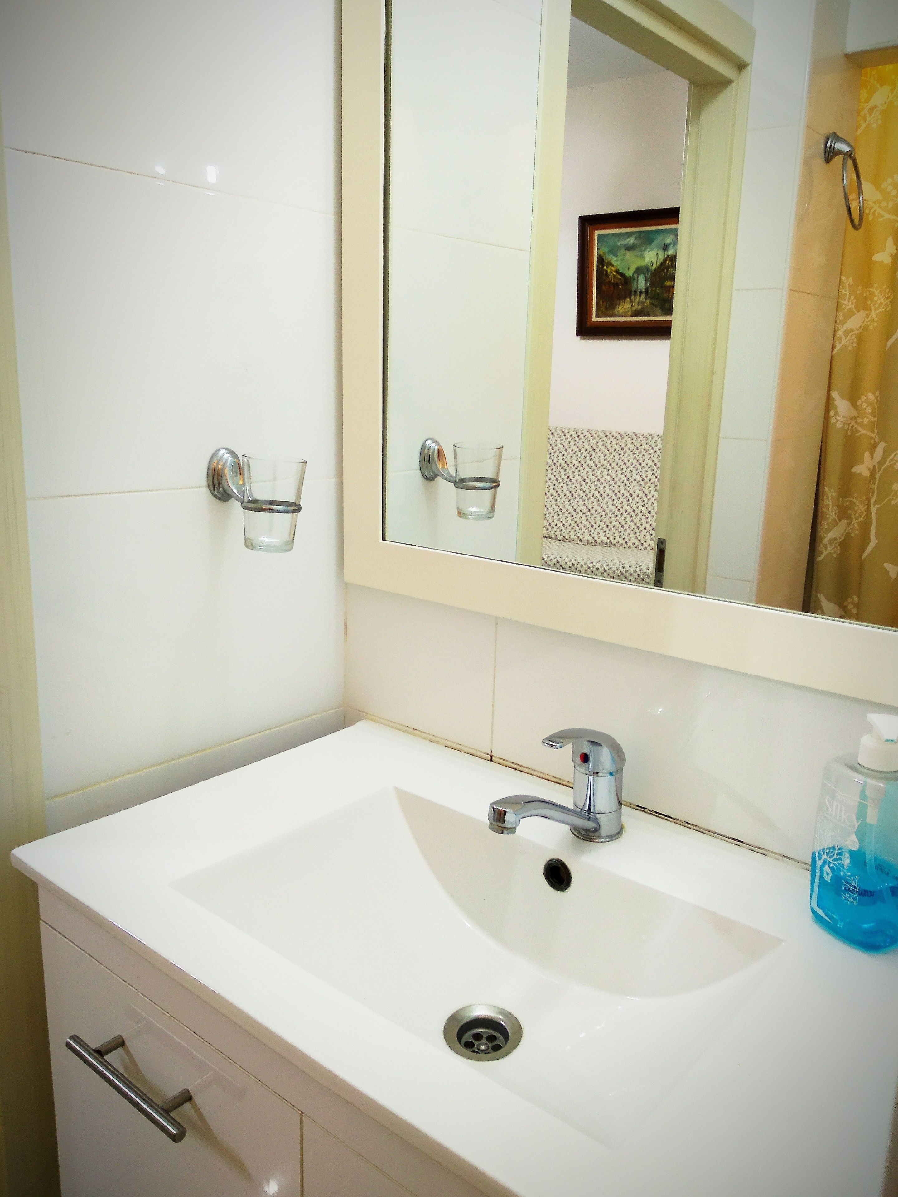 A bathroom with a white sink, a mirror, a glass soap dispenser, and a towel rack.