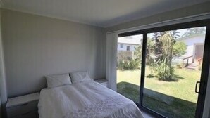 Ein Schlafzimmer mit einem Bett, einem Nachttisch und einer Glasschiebetür, die in einen Garten führt.
