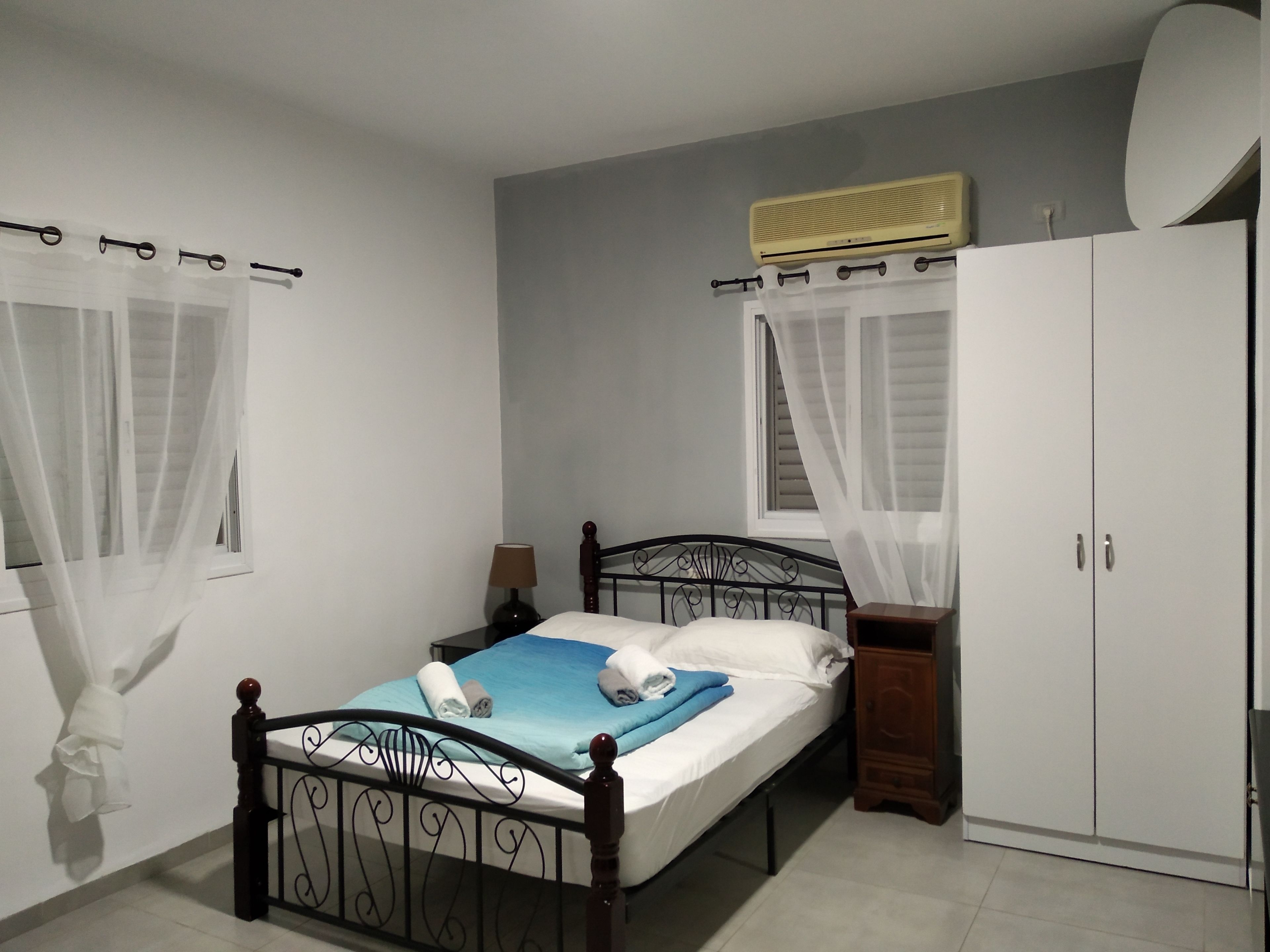 A bedroom with a bed, a bedside table, a wardrobe, and a window with curtains.
