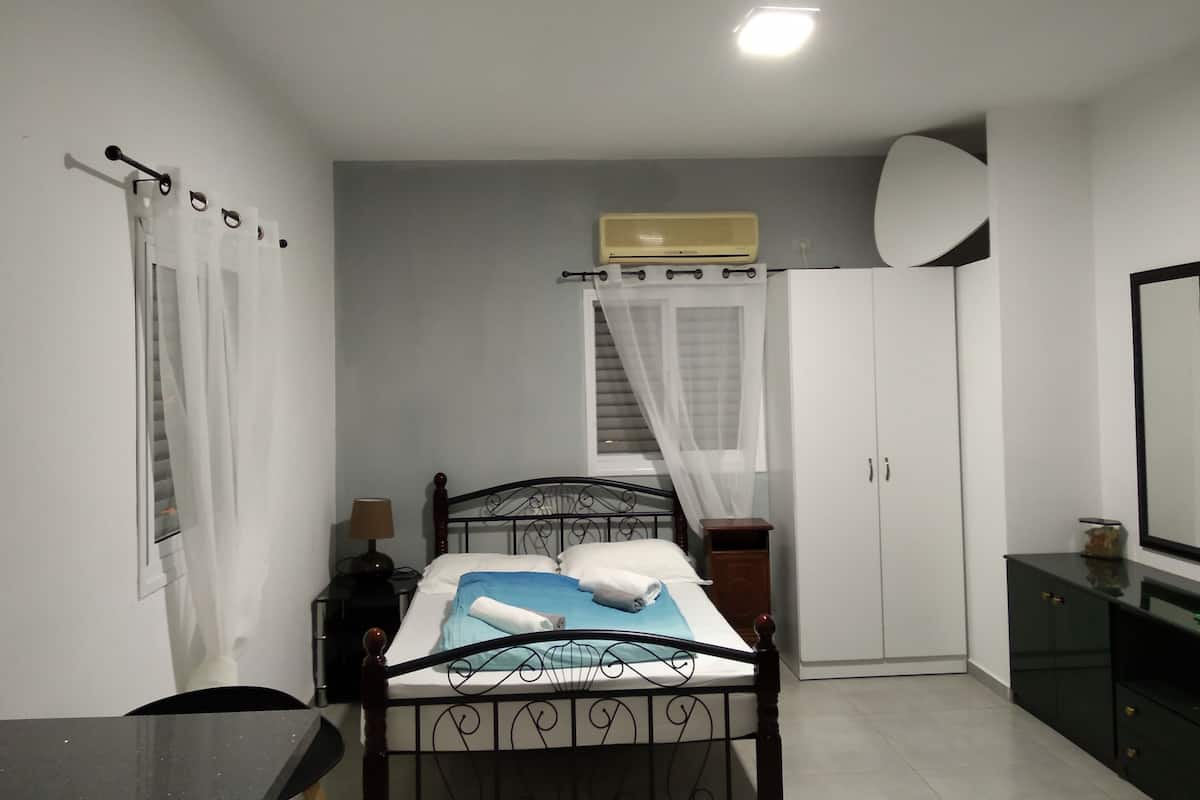Et soveværelse med seng, et natbord, en lampe, et klædeskab og en ventilator.
