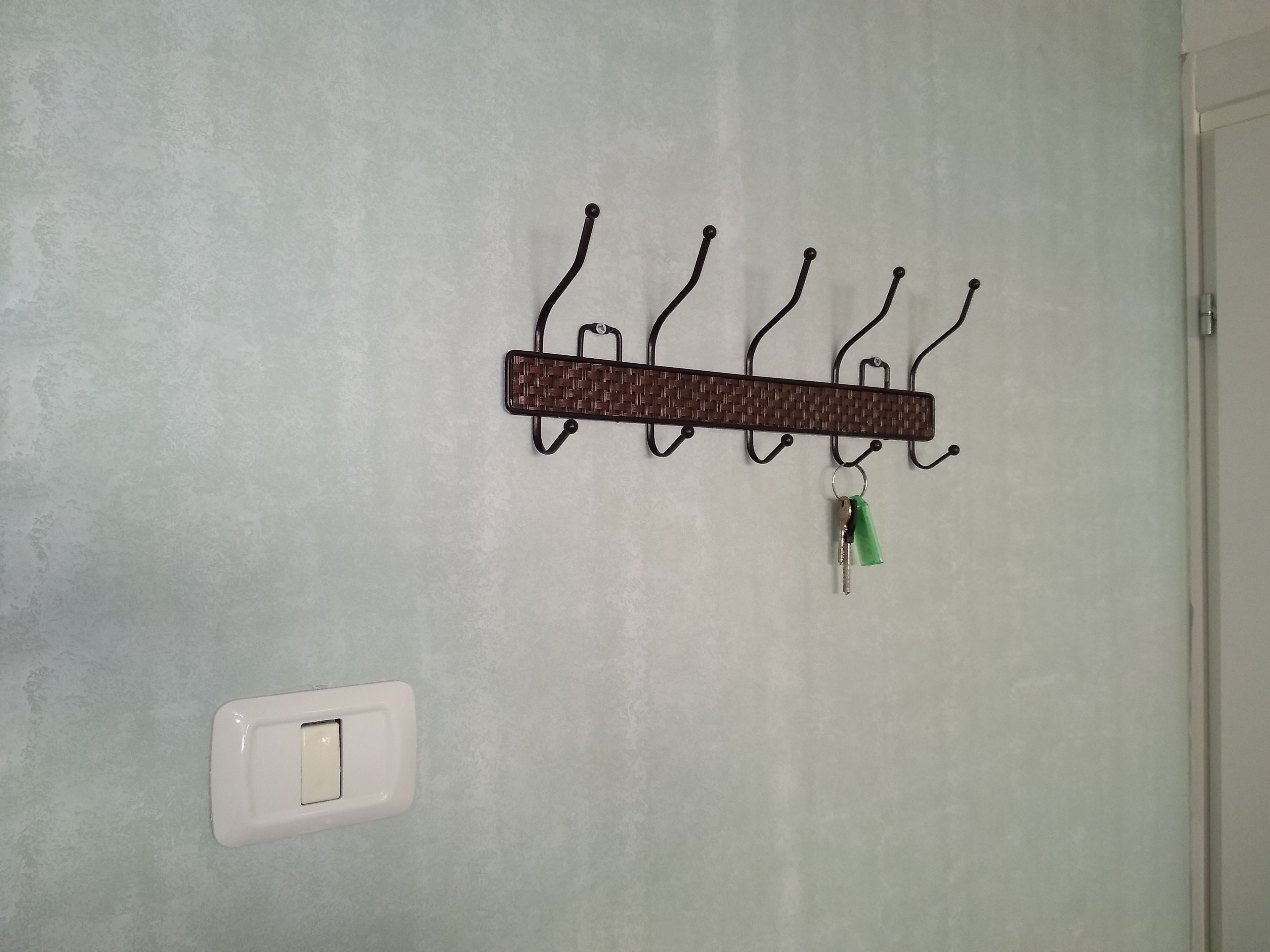 A wall-mounted metal hookboard with a woven rectangular plaque and a single key hanging from it.
