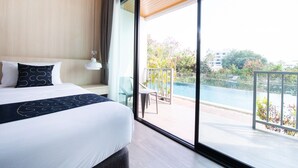 A modern hotel room with a large bed, a view of a swimming pool, and a balcony with a chair.