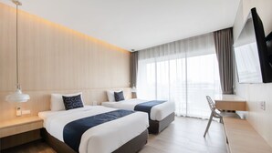 A hotel room with two beds, a desk, a chair, and a TV mounted on the wall.