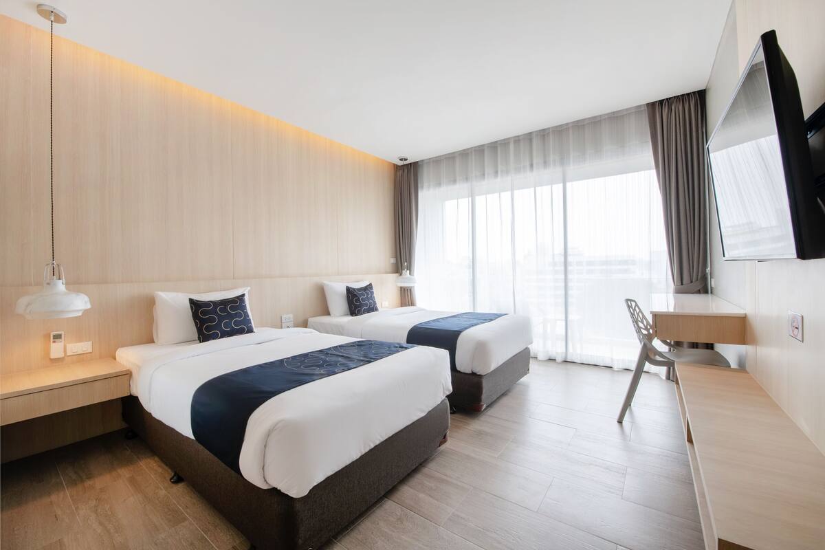 Ein Hotelzimmer mit zwei Betten, einem Schreibtisch, einem Sessel und einem an der Wand montierten Fernseher.