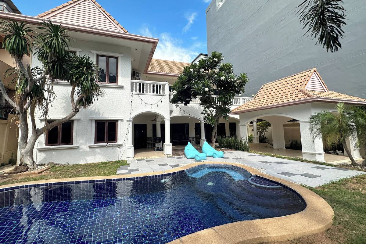 Ein zweistöckiges Haus mit Schwimmbad, umgeben von Palmen und einer überdachten Terrasse.