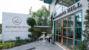 A building with a sign reading "Blooming Hill Boutique Suites" and a patio area with outdoor seating.