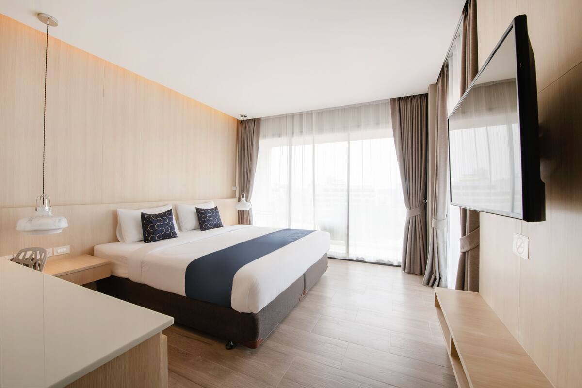 Ein modernes Hotelzimmer mit einem großen Bett, Nachttischen, einem Schreibtisch und einem an der Wand montierten Fernseher.