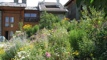A building with a wooden facade and a balcony, surrounded by a garden with various wildflowers.