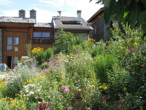 Un bâtiment à la façade en bois et doté d’un balcon, entouré d’un jardin où poussent différentes espèces de fleurs sauvages.