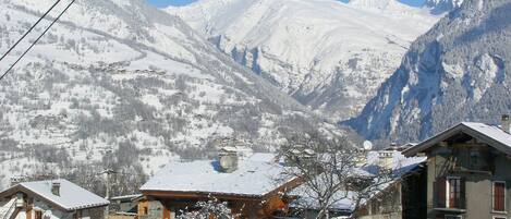 A snow-covered mountain village with traditional wooden houses, a clear sky, and a view of the surrounding peaks.