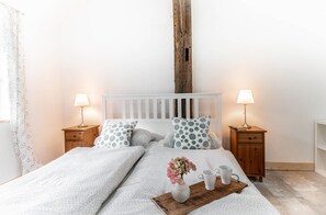 A neatly made bed with a white headboard, two bedside tables with lamps, a wooden nightstand, and a tray with a vase and two cups.