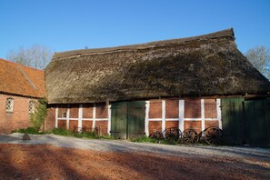 A rustic building with a thatched roof, brick walls, and a dirt road in front.