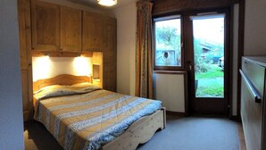 Una camera da letto con un letto in legno, una finestra con tende e una porta che dà sull'esterno.