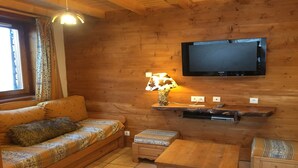 Accogliente camera in legno con divano, un tavolino, una lampada e TV a parete.