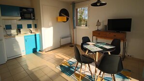 Cocina compacta con microondas, pileta y alacenas. Cuenta con un comedor con mesa y sillas, y un televisor sobre un mueble de madera.