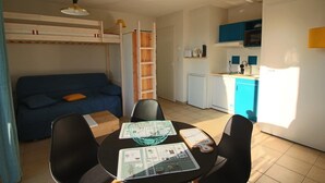 Un espacio habitable compacto con literas, kitchenette, zona de comedor con mesa y sillas, y sofá.