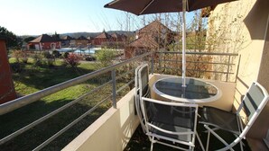 Un balcón con mesa y sillas de vidrio, baranda de metal y vista a una zona residencial con casas y una piscina.