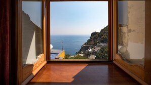 Ein Zimmer mit großem Fenster und Blick auf das Meer sowie eine gebirgige Landschaft.