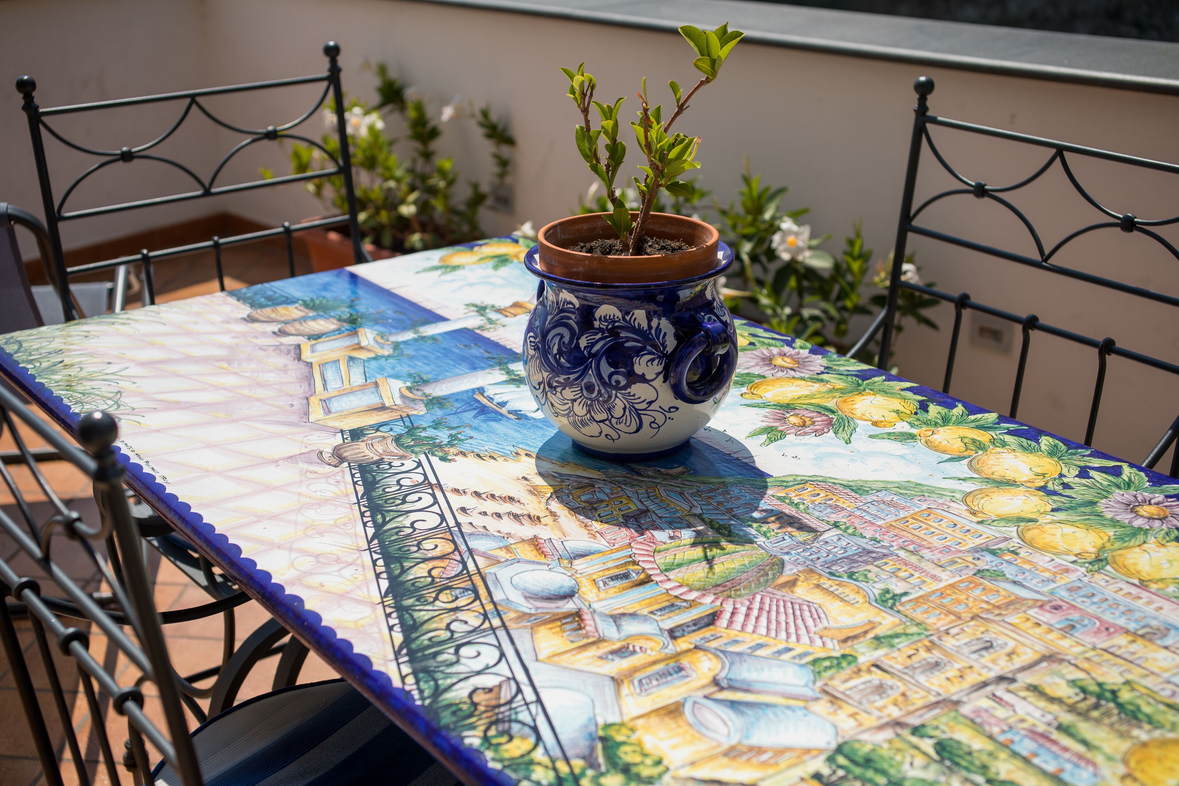 A table with a colorful tablecloth featuring a cityscape design, a potted plant, and a metal chair.