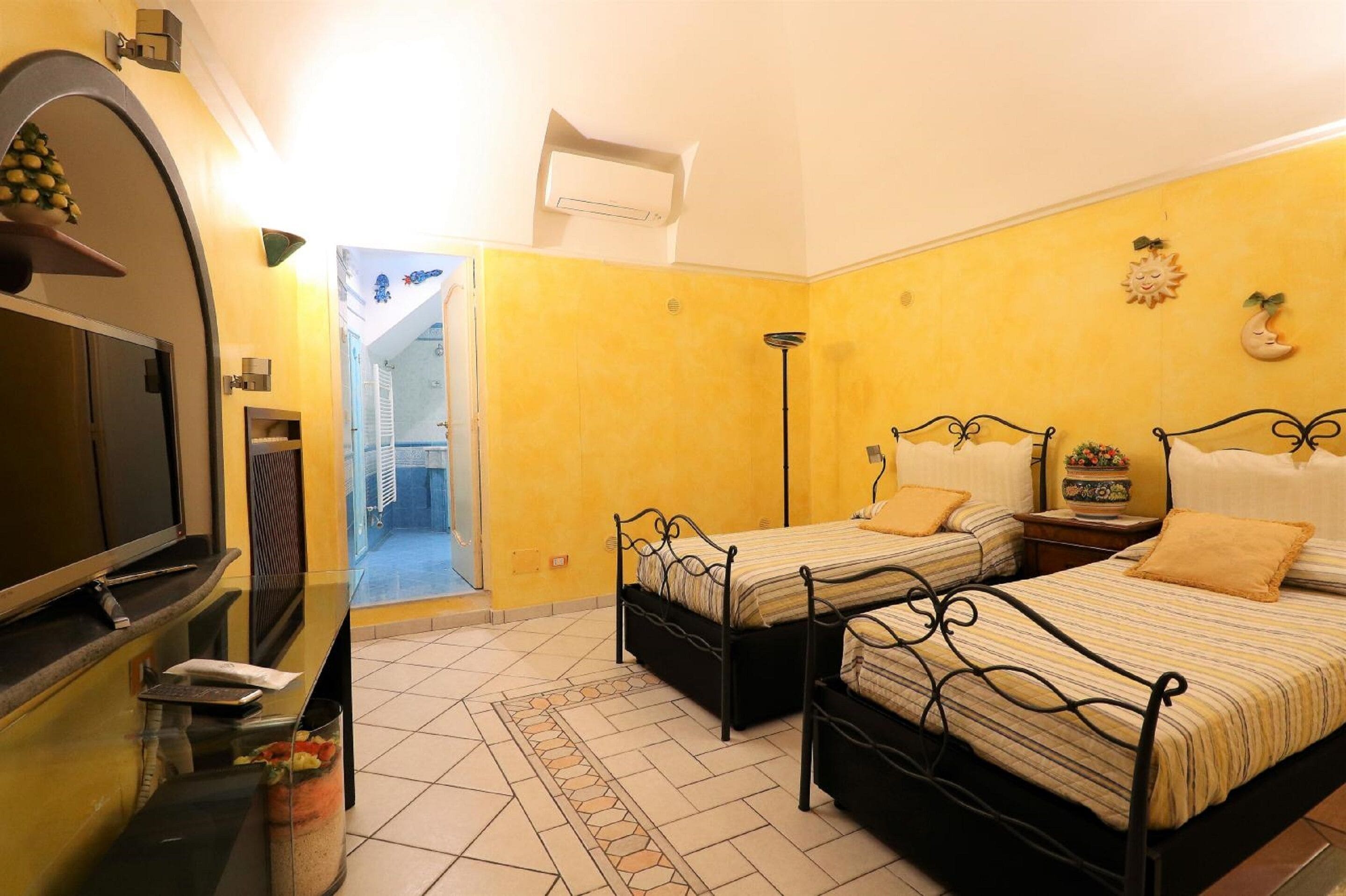 Une chambre d’hôtel avec deux lits, une télévision, une petite table et une salle de bain visible à travers une porte ouverte.