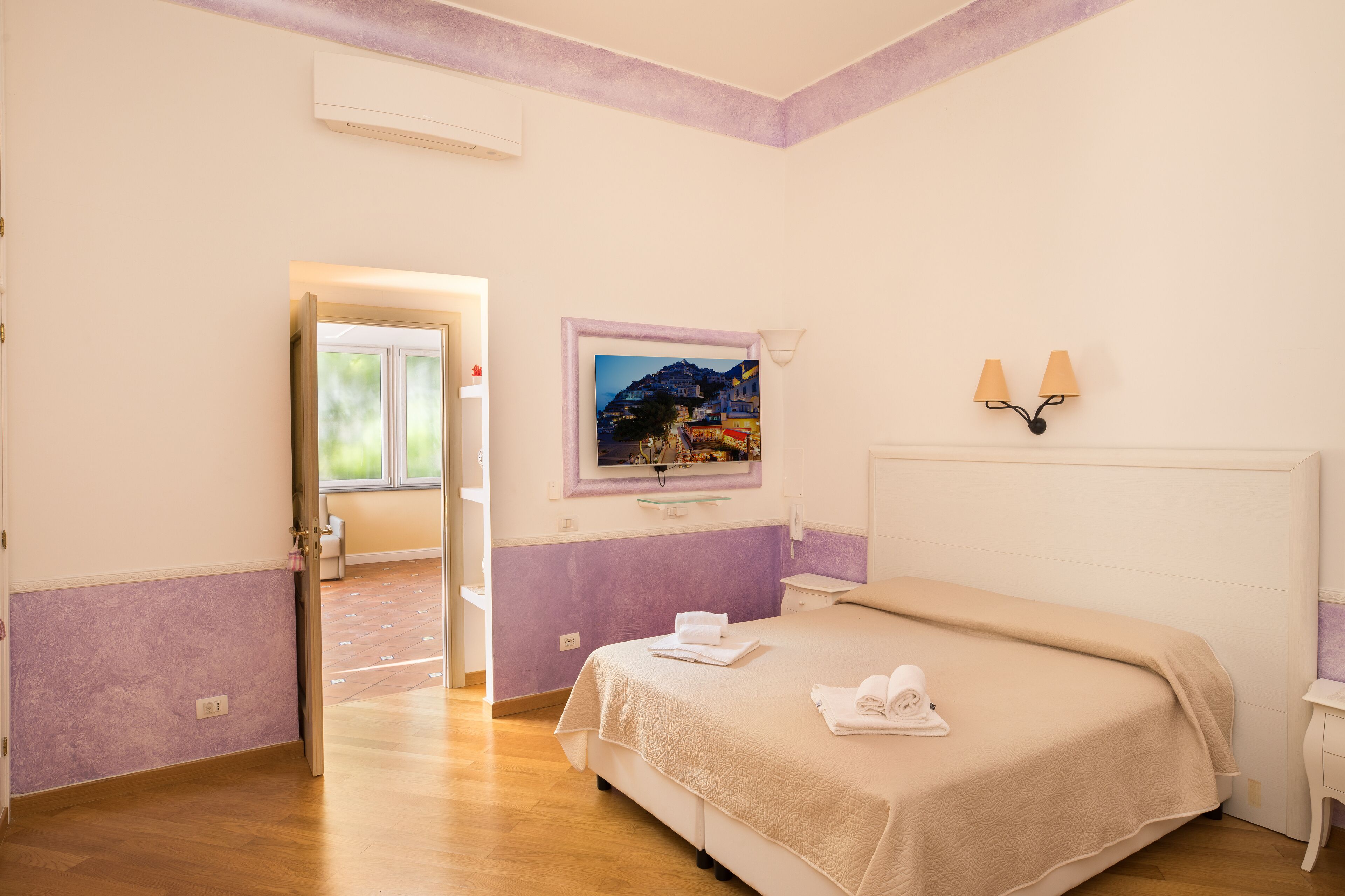 A bedroom with a bed, a nightstand, a wall-mounted lamp, and a window with a view of a mountain.
