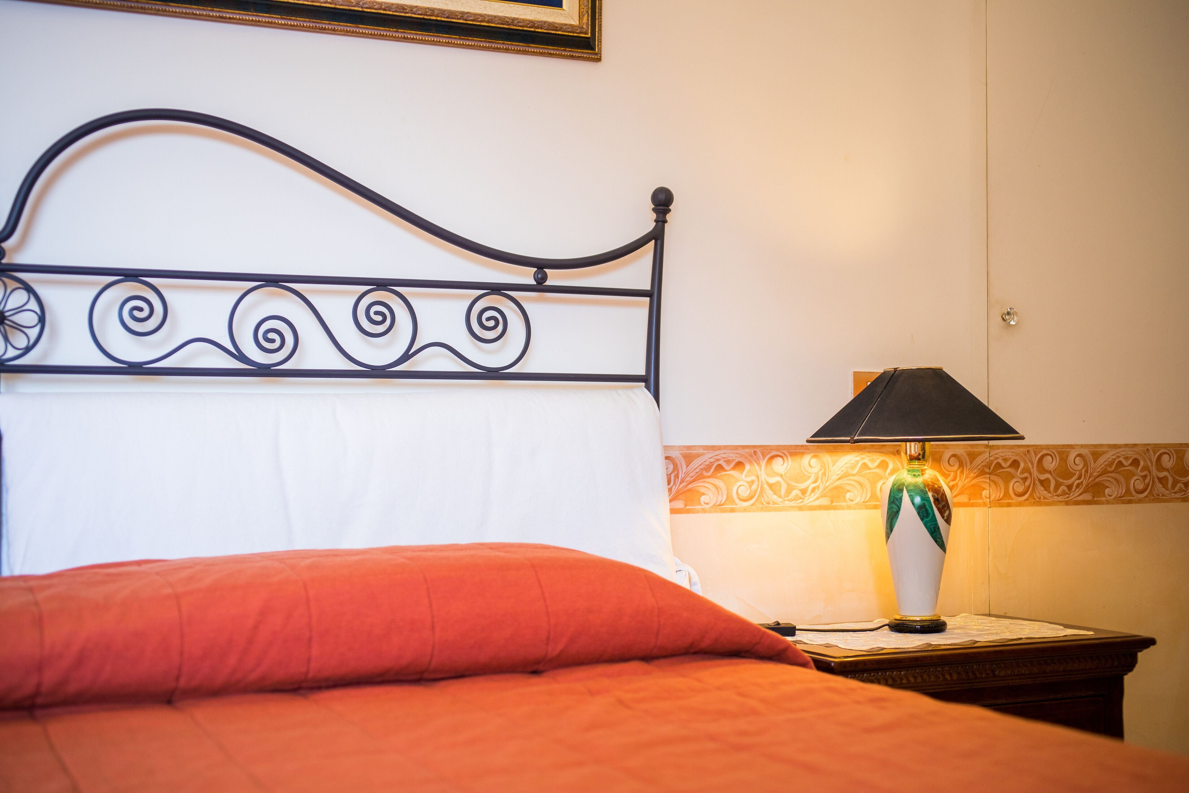 A bed with a metal headboard, a red pillow, and a nightstand with a lamp.