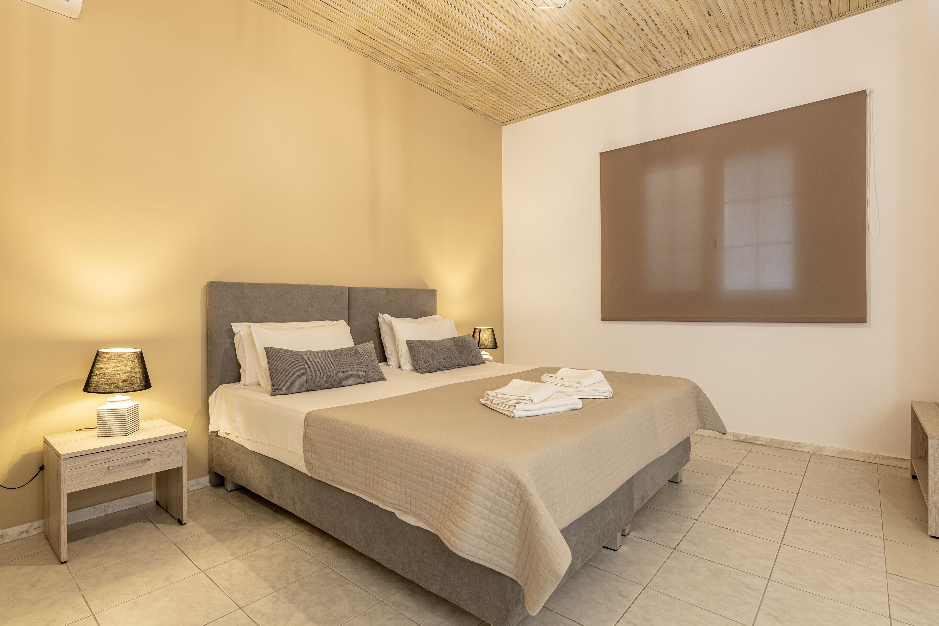 A bedroom with a bed, nightstand, lamp, and a large window.