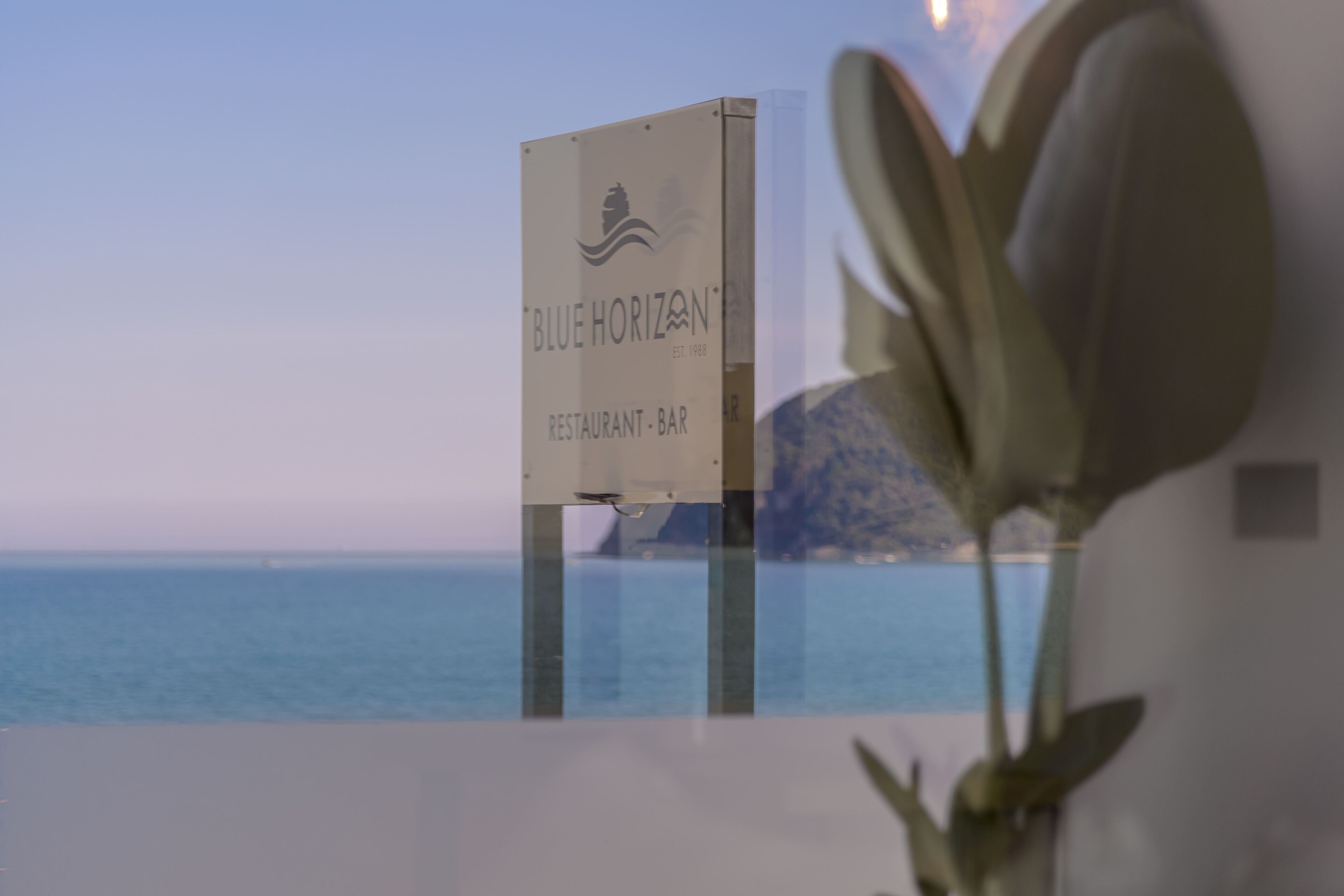 A sign for 'Blue Horizon Restaurant-Bar' with a view of the sea.