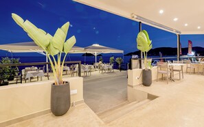 An outdoor dining area with tables and chairs, potted plants, and a view of the sea at dusk. - Blue Horizon Studios (Zakynthos)