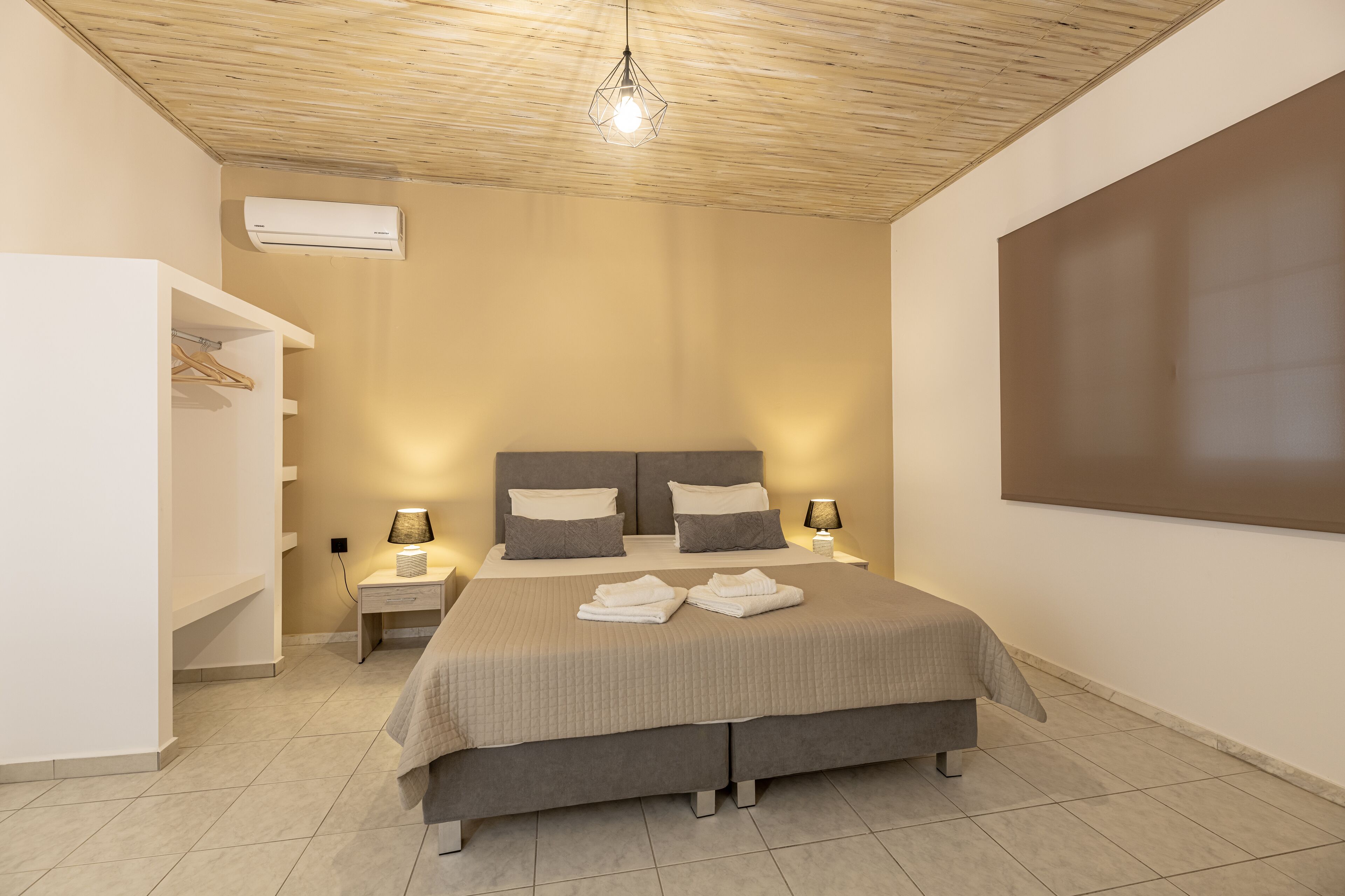 A bedroom with a large bed, bedside tables, a wardrobe, and an air conditioning unit.
