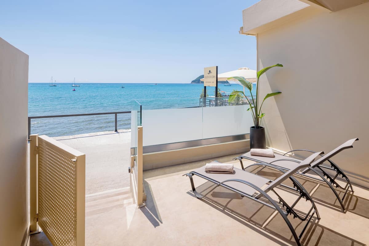 A balcony with a view of the sea, a potted plant, and two lounge chairs.