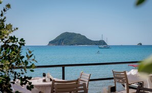 A seaside restaurant with tables and chairs, a view of the sea, and a distant island. - Blue Horizon Studios (Zakynthos)