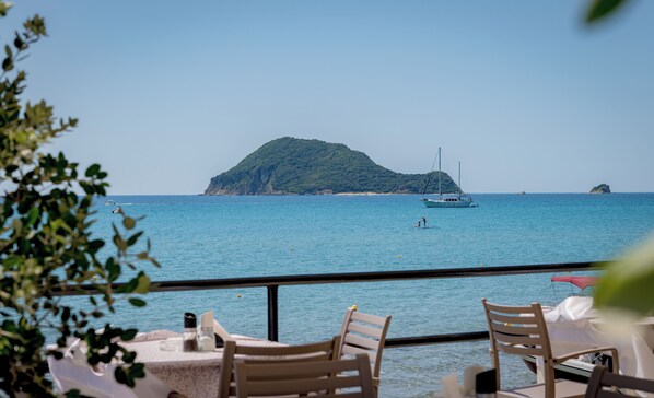 A seaside restaurant with tables and chairs, a view of the sea, and a distant island.