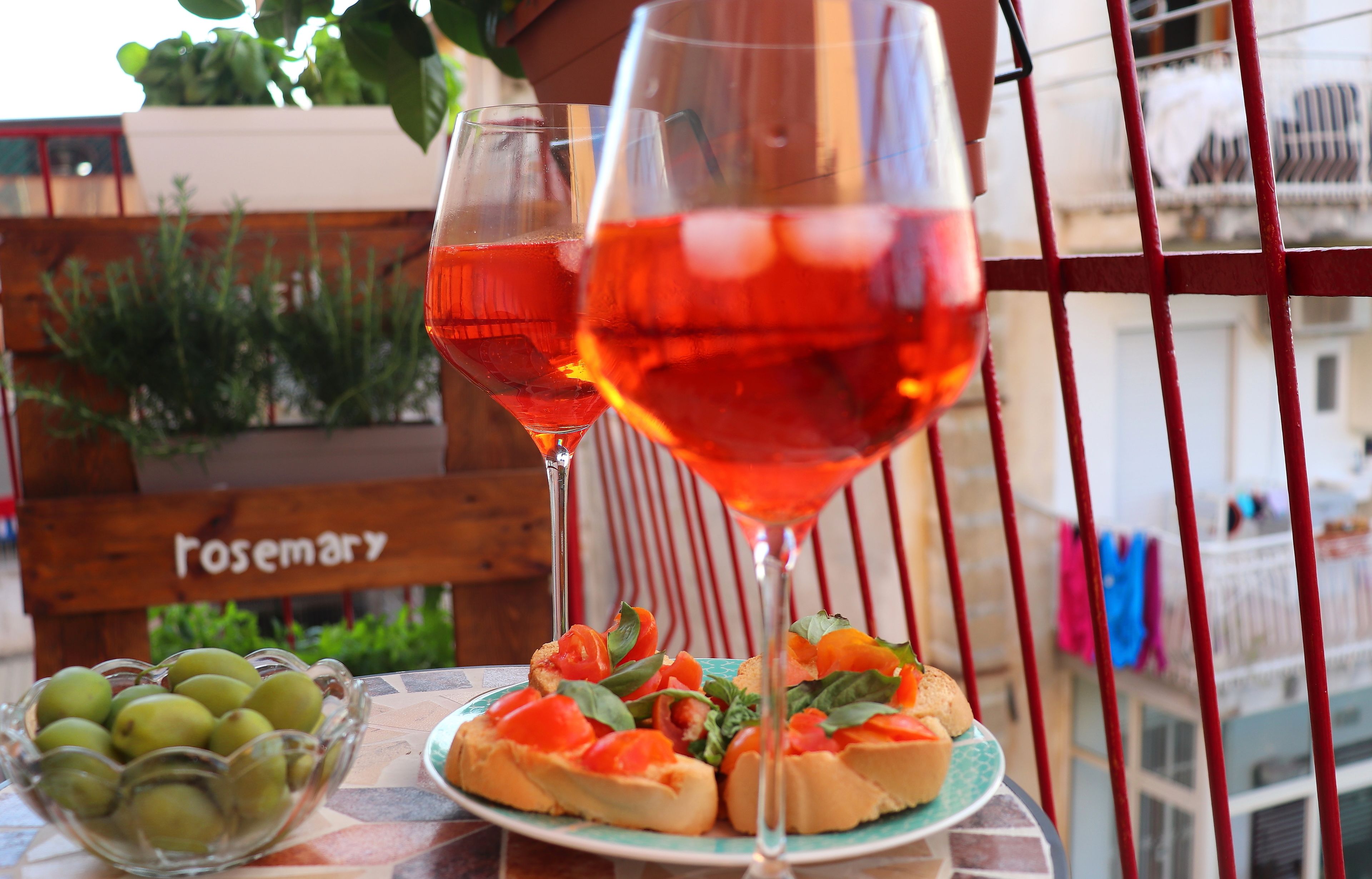 A table with a plate of bruschetta and a bowl of olives, two glasses of red wine, and a wooden chair labeled "Rosemary".
