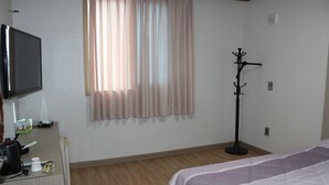 Una habitación de hotel con una cama, televisor, perchero y una ventana con cortinas.
