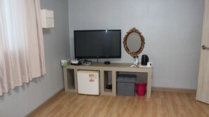Una habitación pequeña con televisión, espejo, refrigerador y un cubo de basura.