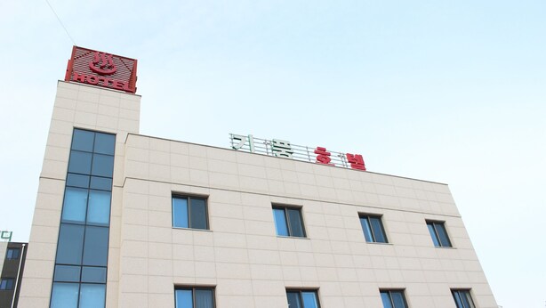 Un edificio de hotel con diseño moderno, que presenta un logotipo rojo llamativo en la parte superior y un cartel con texto coreano.